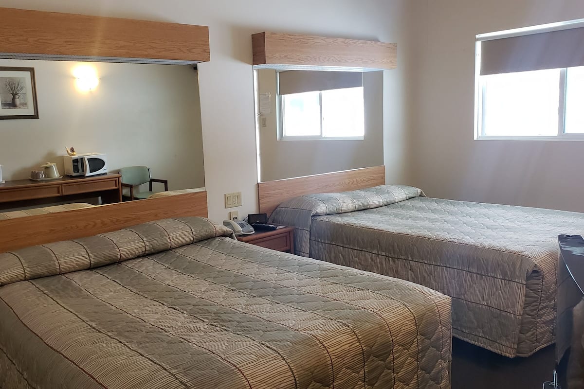 A hotel room with two beds, a small desk with a chair, a microwave, and a nightstand.