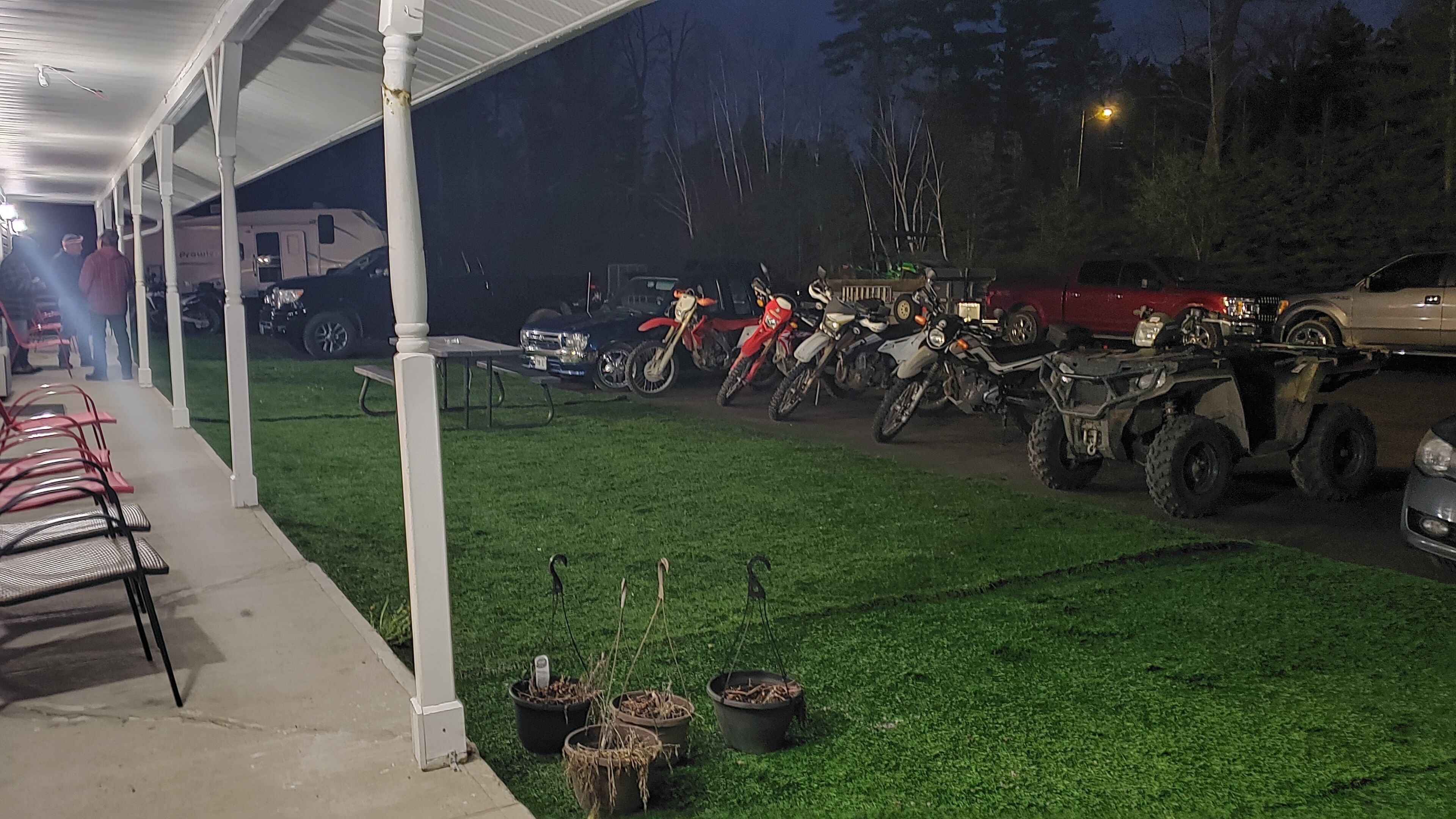 Un espacio exterior cubierto con césped artificial, plantas en macetas y varias motocicletas y cuatrimotos estacionadas.