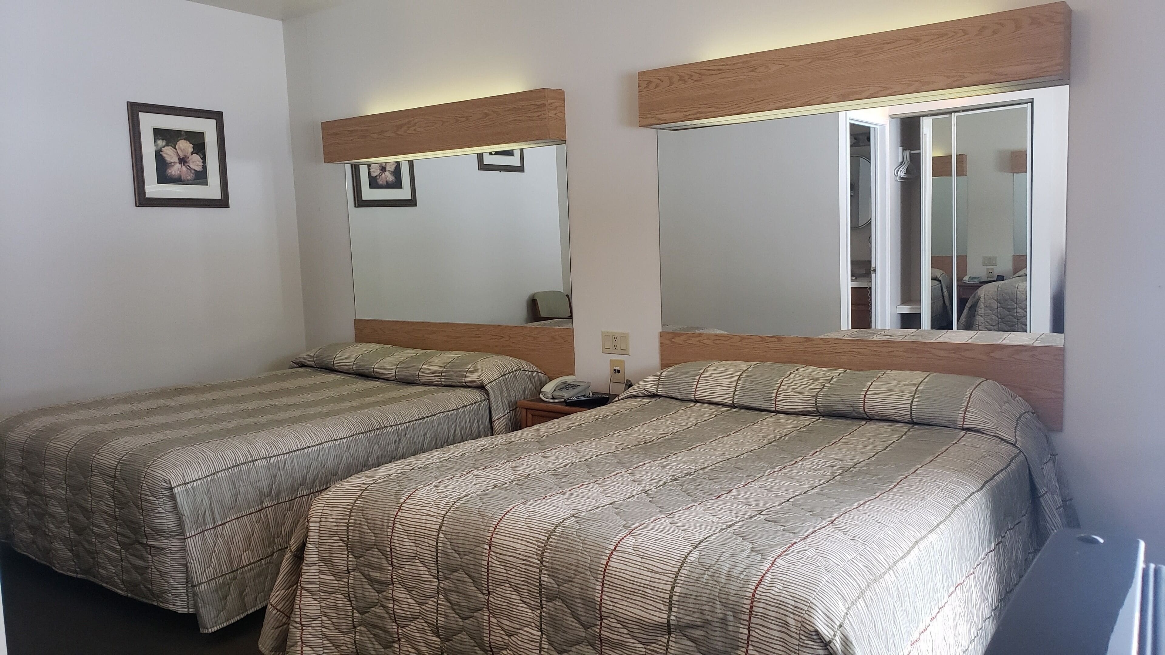 Een hotelkamer met twee eenpersoonsbedden, een nachtkastje met een telefoon en een spiegel die de kamer weerkaatst.