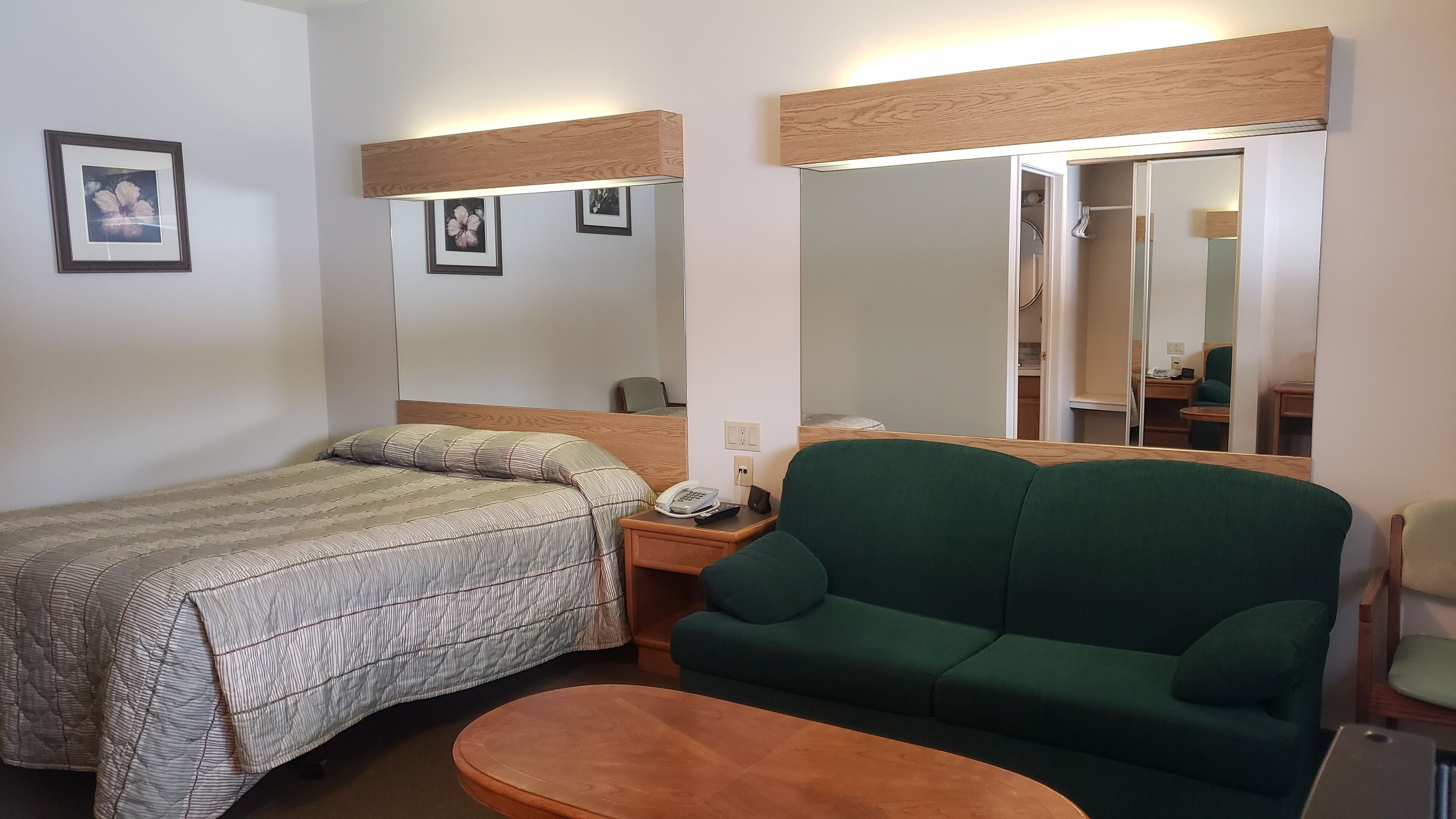 A hotel room with a bed, a green sofa, a small round table, a mirror, and a telephone on the nightstand.