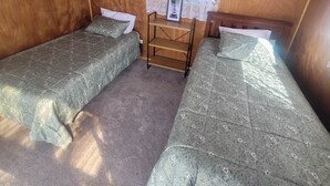 Ett litet, ombonat rum med två enkelsängar, en trähylla med en inramad tavla och ett fönster med spetsgardiner.