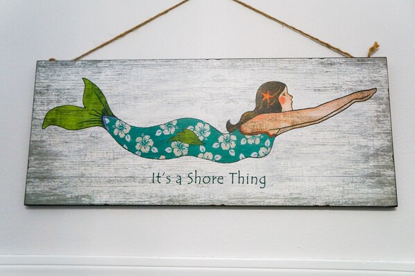 Un letrero de madera con una ilustración de una sirena y el texto 'It's a Shore Thing'.