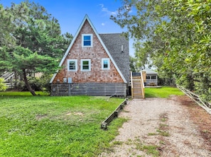 A wooden cabin with a triangular roof, a small porch, and a gravel path leading to the entrance.