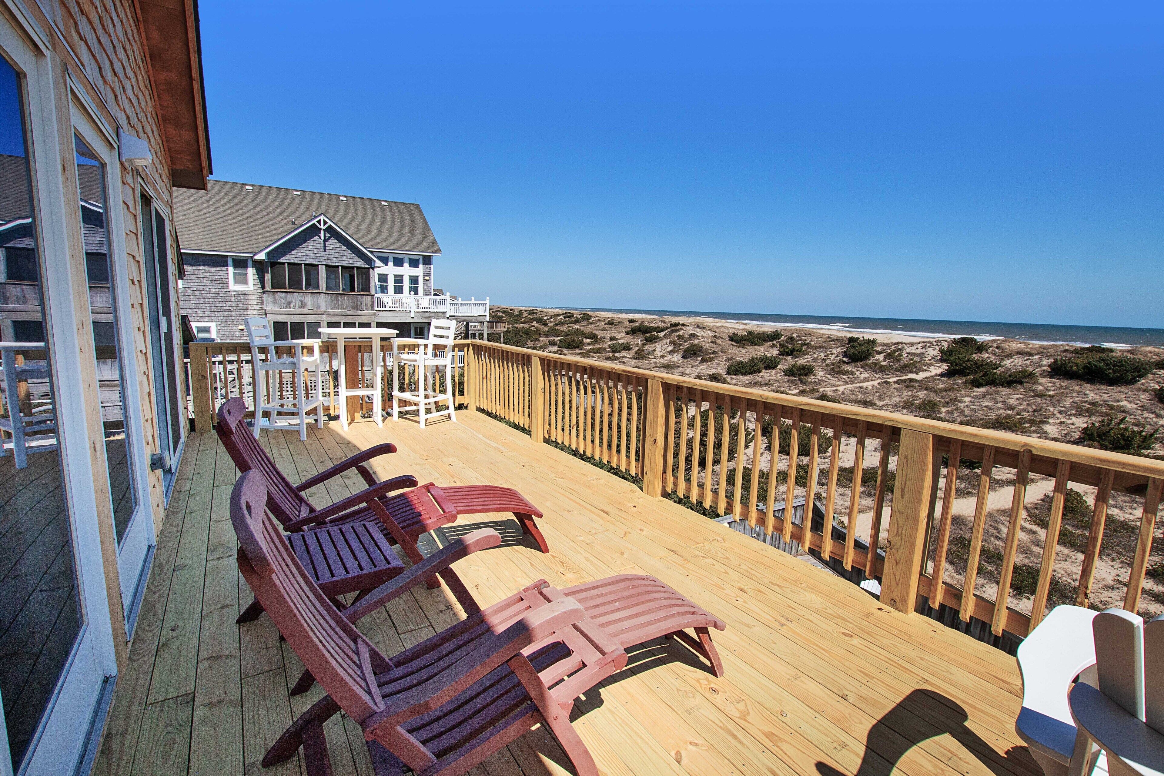 A wooden deck with lounge chairs overlooking a beach.