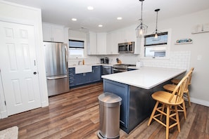 A modern kitchen with white cabinets, stainless steel appliances, a wooden floor, and a central island with bar stools.