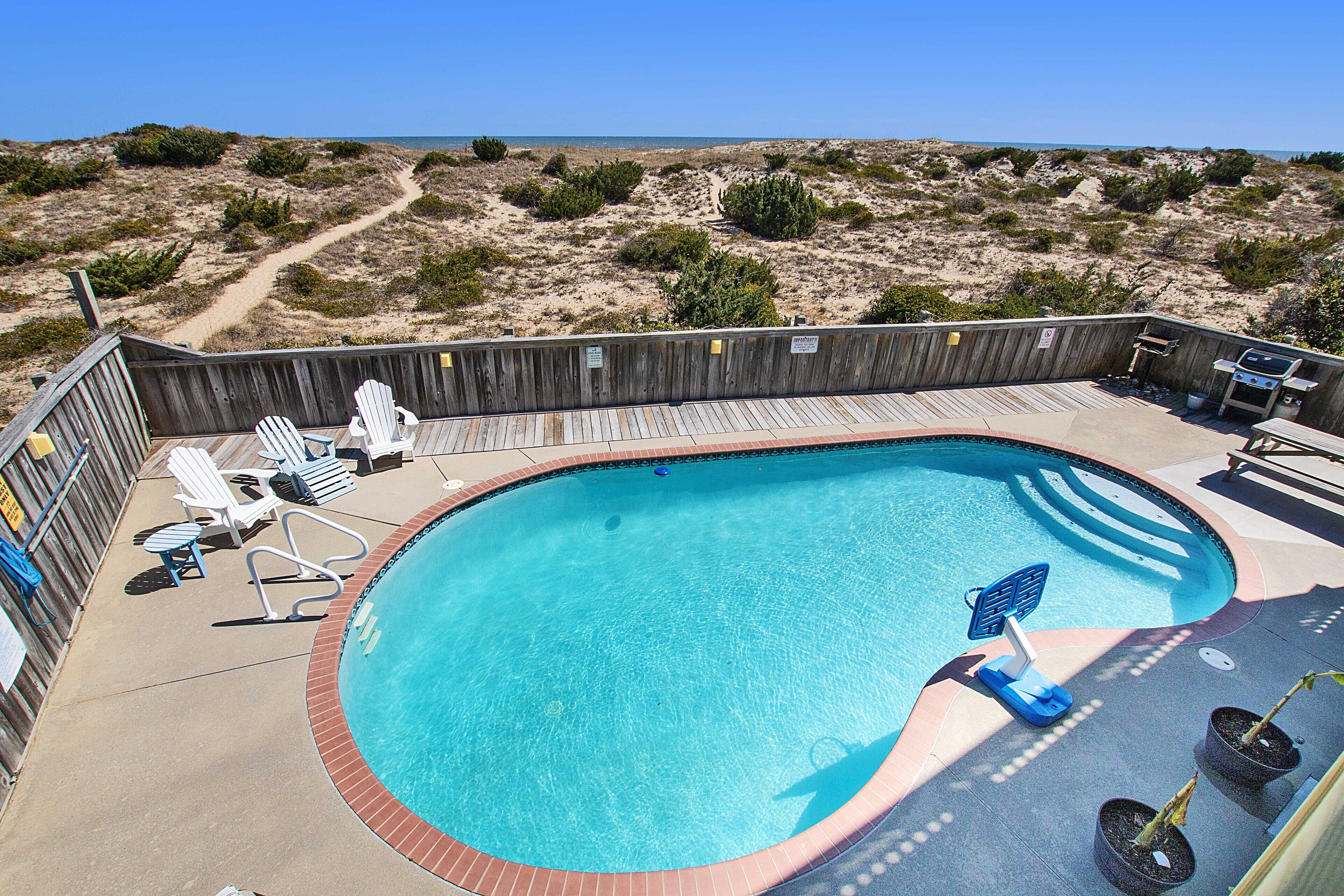En swimmingpool med træterrasse, liggestole og grillområde.