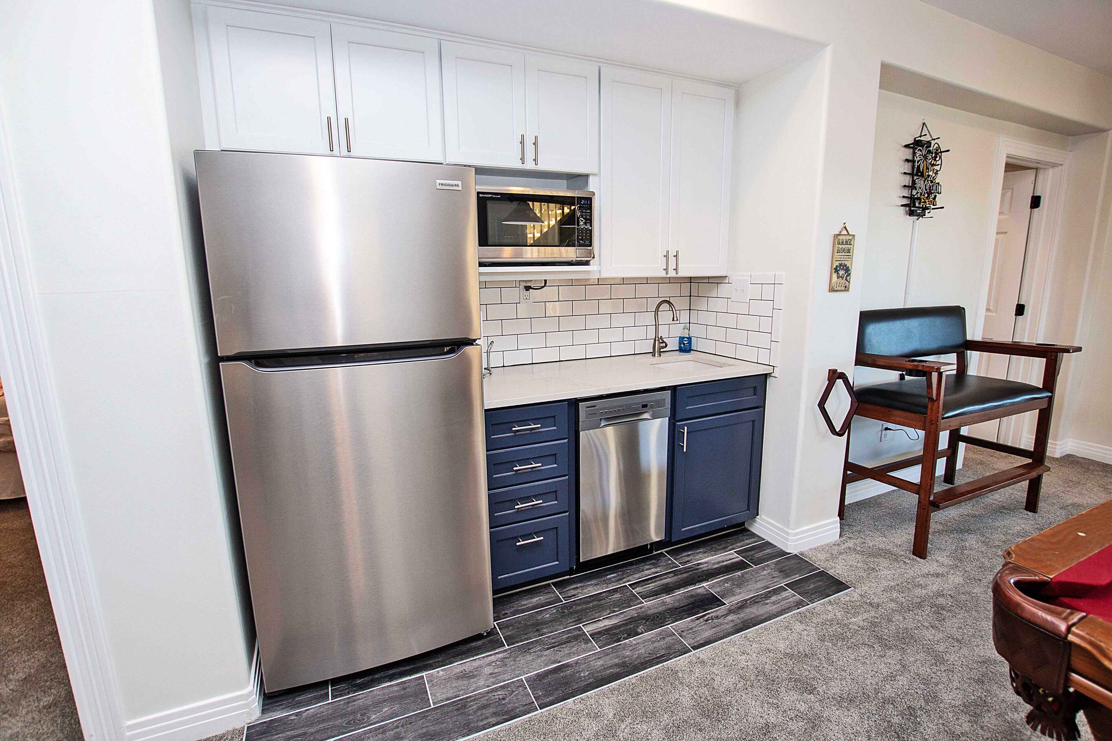 A kitchen with white cabinets, a stainless steel refrigerator, a dishwasher, and a wooden chair.
