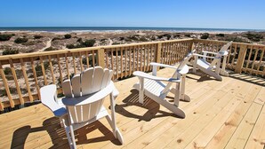 A wooden deck with two white Adirondack chairs facing a beach. - Oceanfront, Beach Access, Private Pool, Hot Tub, & Game Room (Avon)