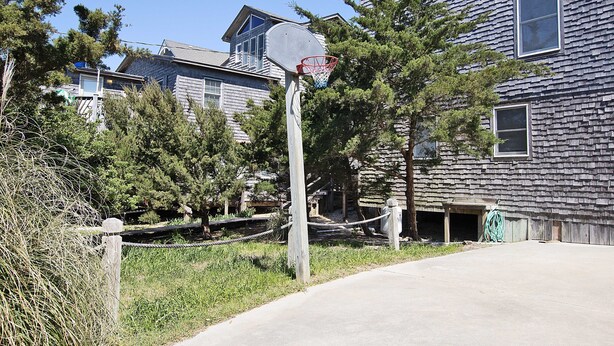 A residential area with a basketball hoop in front of a house with a dark shingled exterior. - Oceanfront, Beach Access, Private Pool, Hot Tub, & Game Room (Avon)