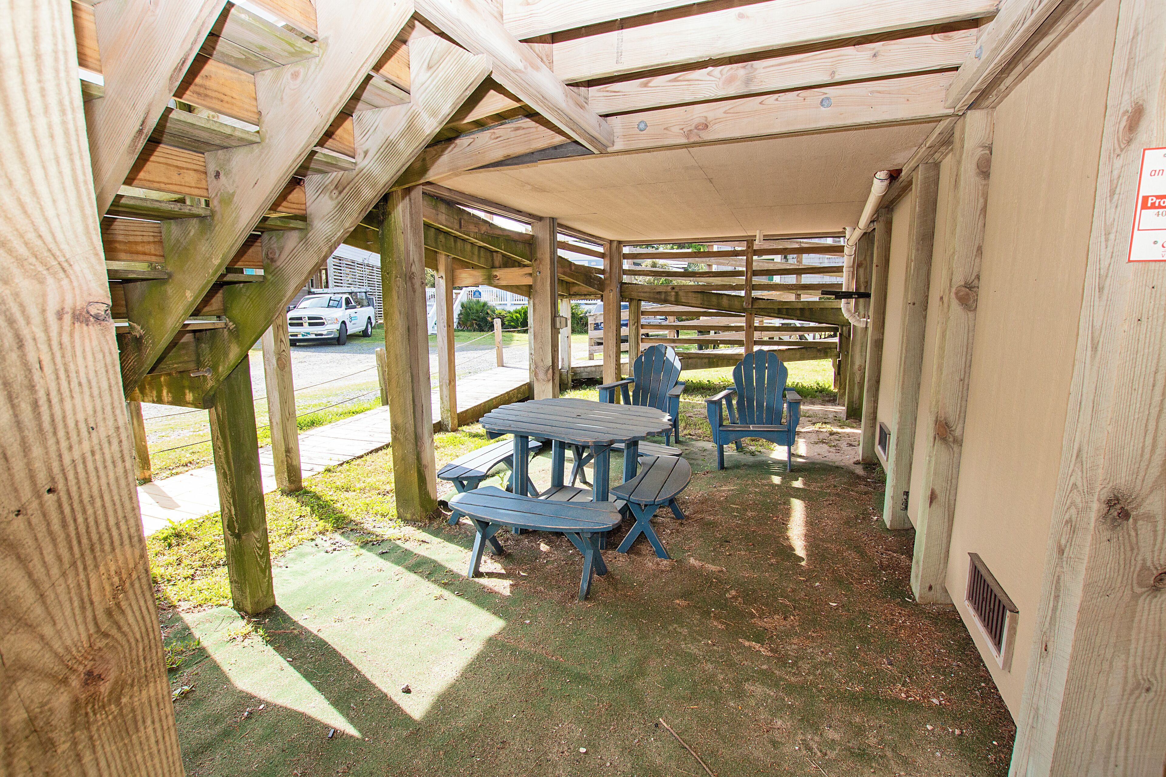 A covered outdoor seating area with picnic tables and chairs, a wooden structure, and a view of a street with a white truck.