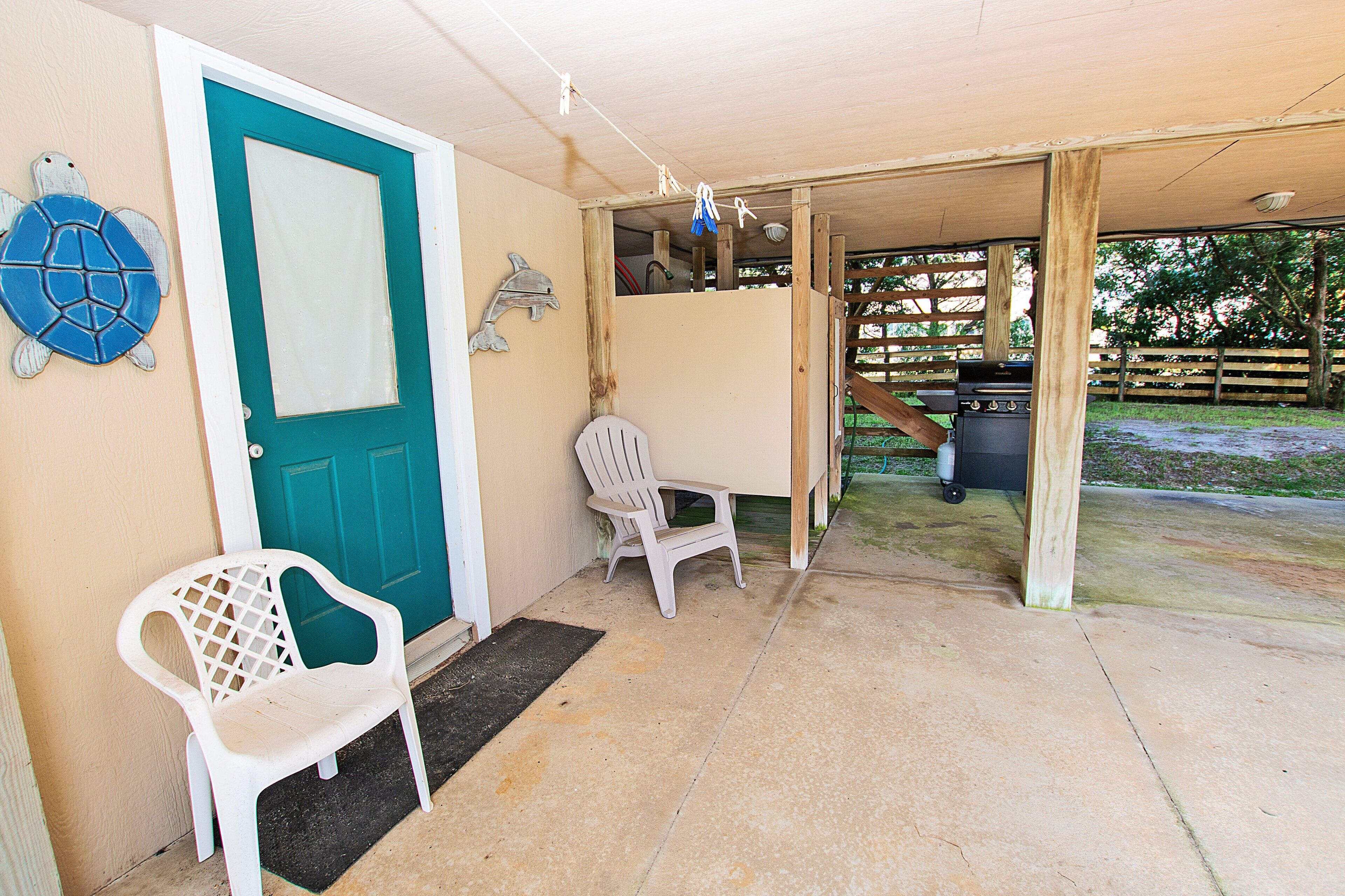 A covered outdoor area with a teal door, a white plastic chair, and a grill.