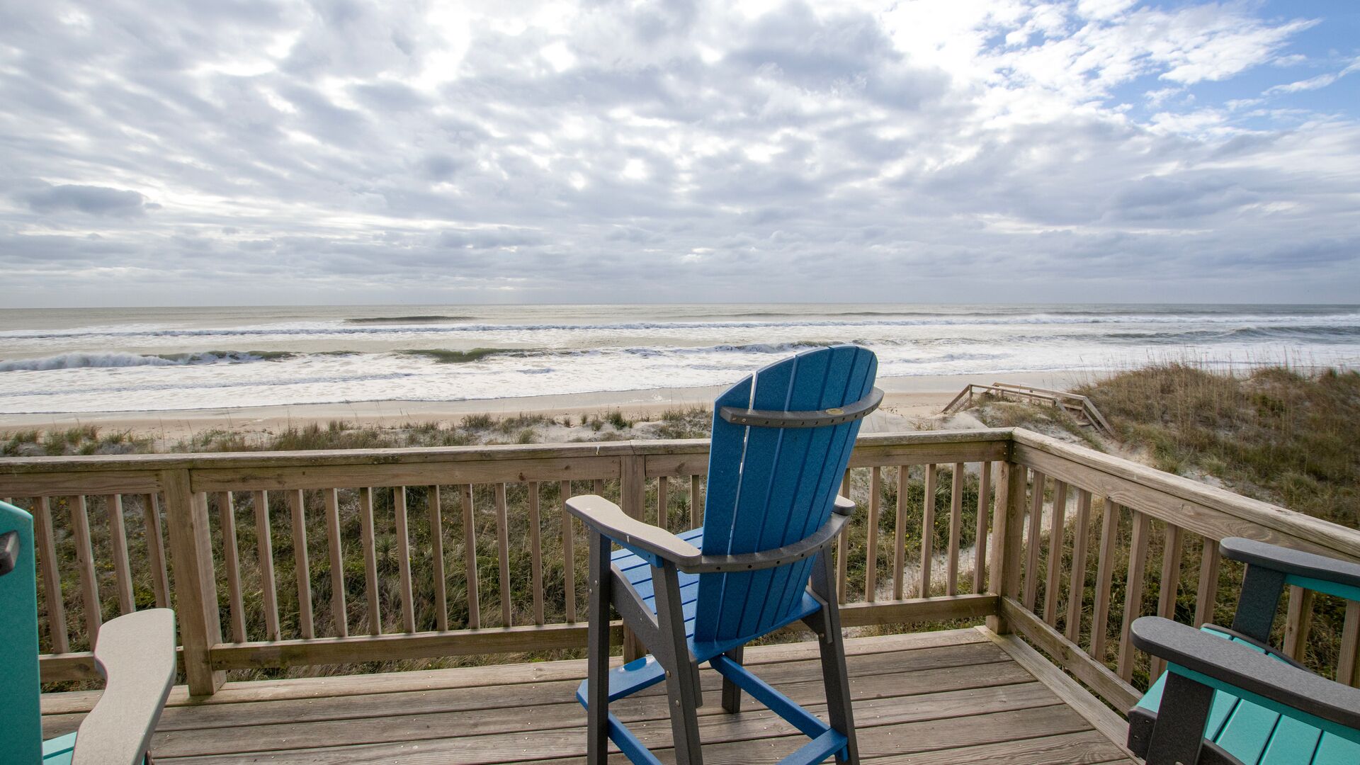 Une terrasse en bois avec une chaise Adirondack bleue donnant sur une plage.