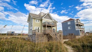 Ett tvåvåningshus som ligger vid stranden, med en träveranda och en trappa som leder upp till övervåningen.