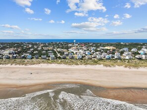 A coastal town with houses along the beach and a water tower in the distance.
