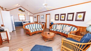 A spacious living area with wicker furniture, a dining table, and a kitchen in the background. - Beachfront, Oceanviews, Dog Friendly, Private Beach Access & Hot Tub (Avon)