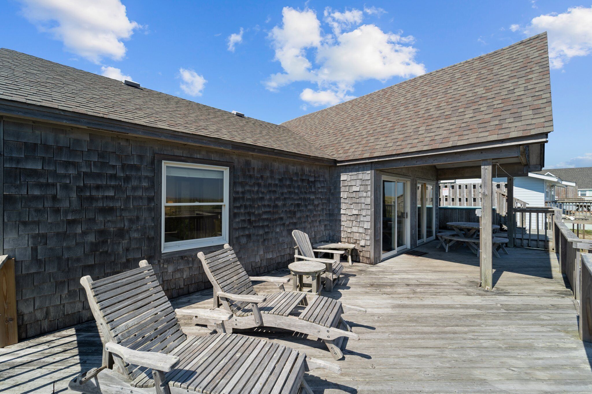 A wooden deck with lounge chairs and a table, a covered patio area, and a building with a dark shingle roof.