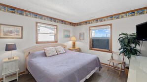 A bedroom with a bed, bedside tables, a lamp, a TV, and a window with a view. - Beachfront, Oceanviews, Dog Friendly, Private Beach Access & Hot Tub (Avon)