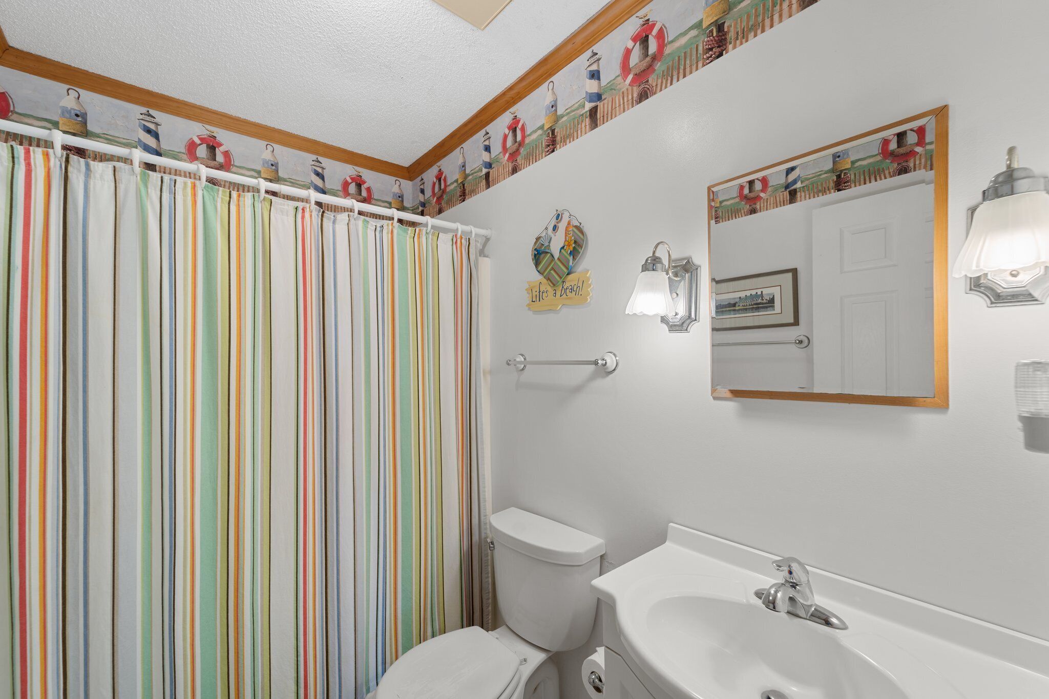 Un bagno con una tenda da doccia a righe, un water, un lavandino e uno specchio.