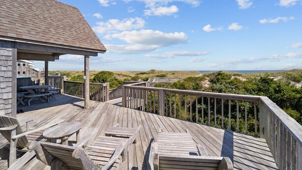 A wooden deck with picnic tables and a covered area, overlooking a beach with dunes and vegetation. - Beachfront, Oceanviews, Dog Friendly, Private Beach Access & Hot Tub (Avon)