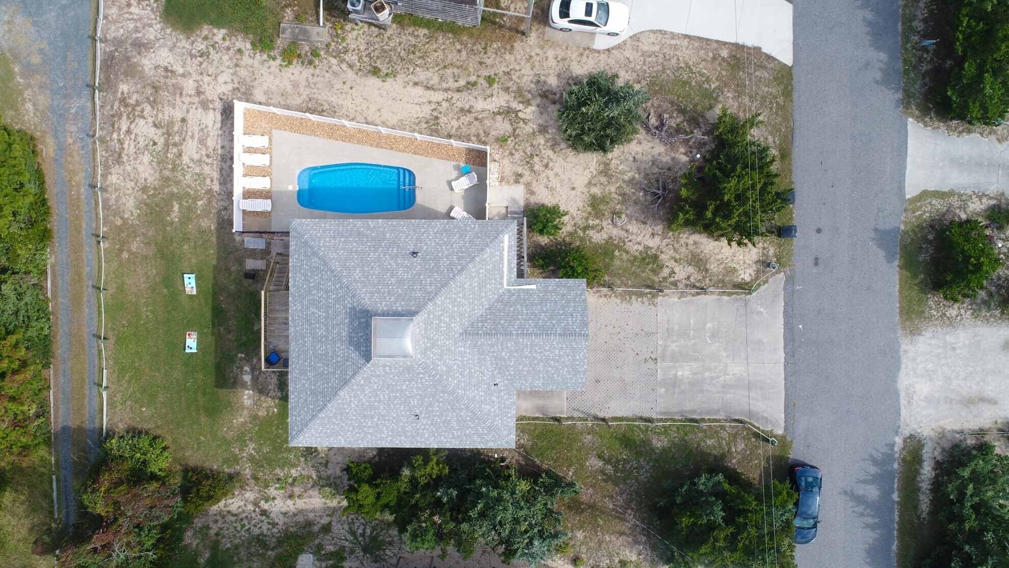 An aerial view of a house with a swimming pool, a fenced yard, and a road nearby.