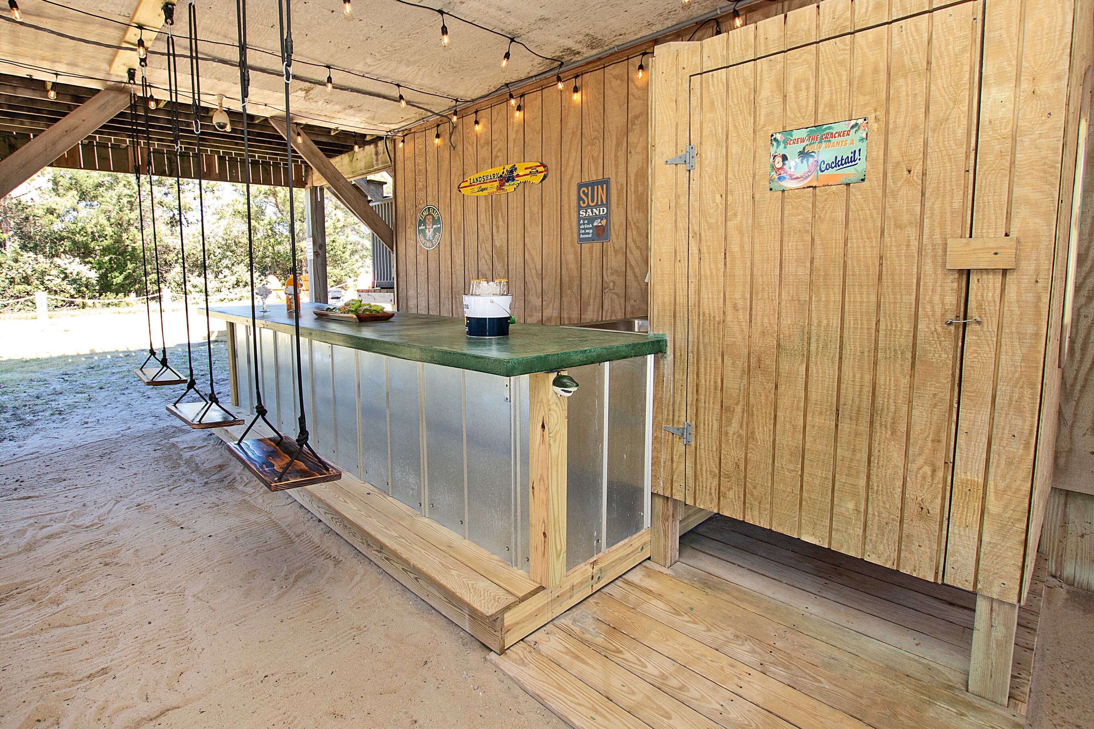 Angolo bar in legno con bancone, luci a sospensione e indicazioni per cocktail.