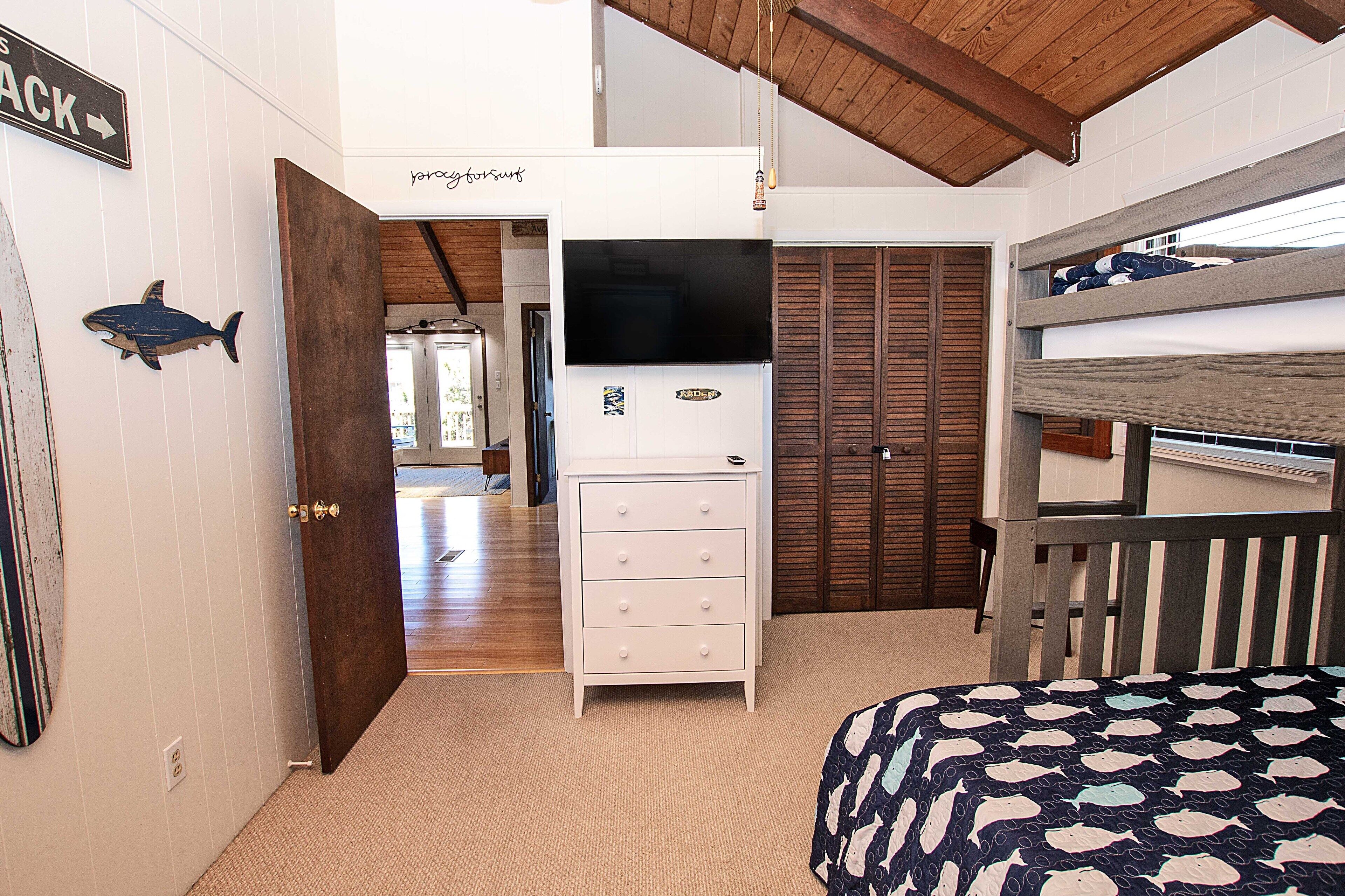 A bedroom with a bunk bed, a dresser, a television, and a door leading to another room.