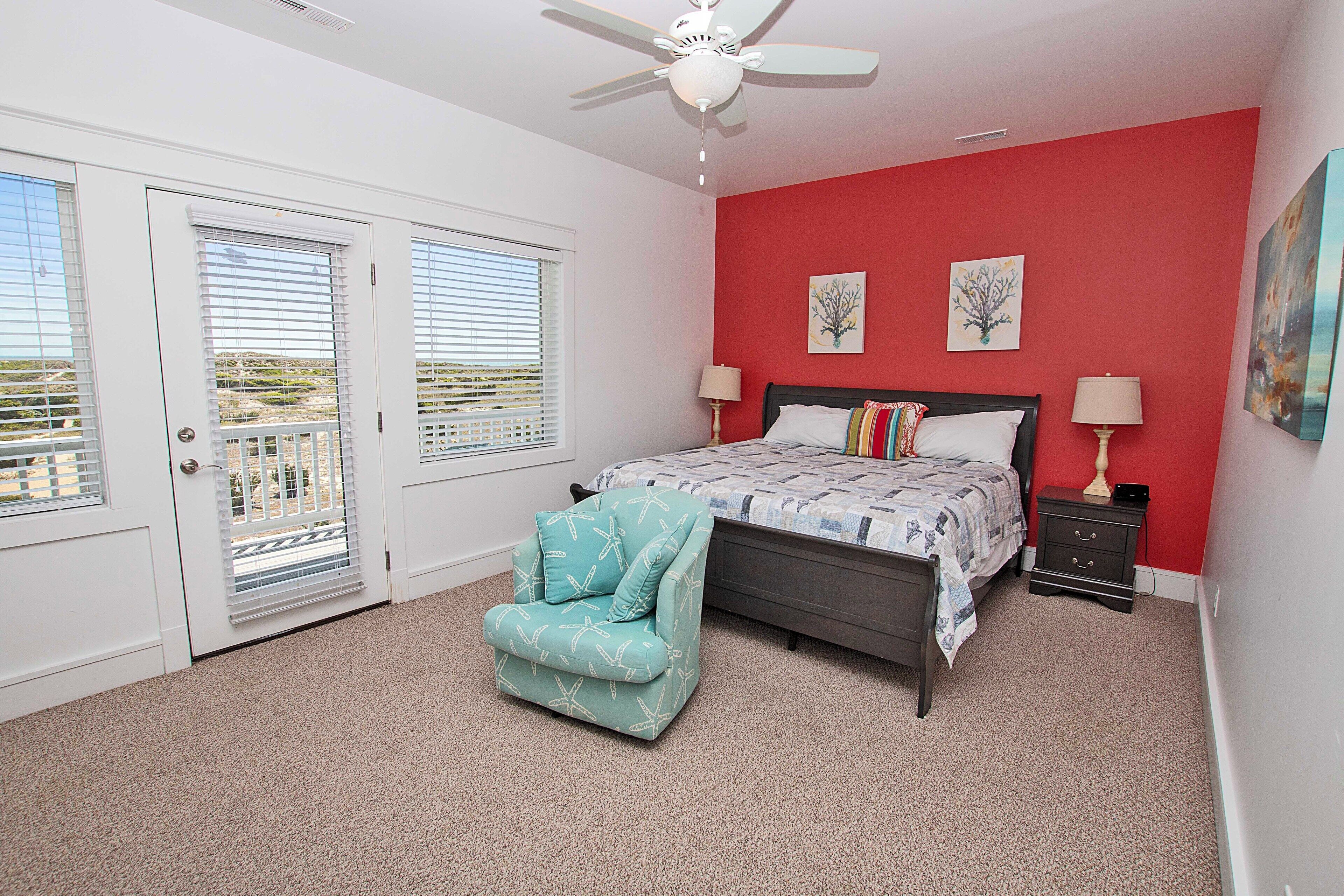 A bedroom with a bed, two nightstands, a chair, a ceiling fan, and two windows with blinds.
