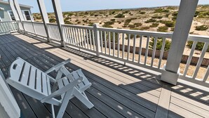 A wooden deck with white railings, a white chair, and a view of a sandy landscape. - Oceanfront, Private Pool, Hot Tub, Theatre, Game Room, & Dog Friendly (Salvo)