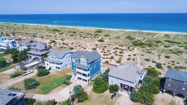 A coastal residential area with multiple two-story houses, a beach, and a clear view of the ocean. - Oceanfront, Private Pool, Hot Tub, Theatre, Game Room, & Dog Friendly (Salvo)