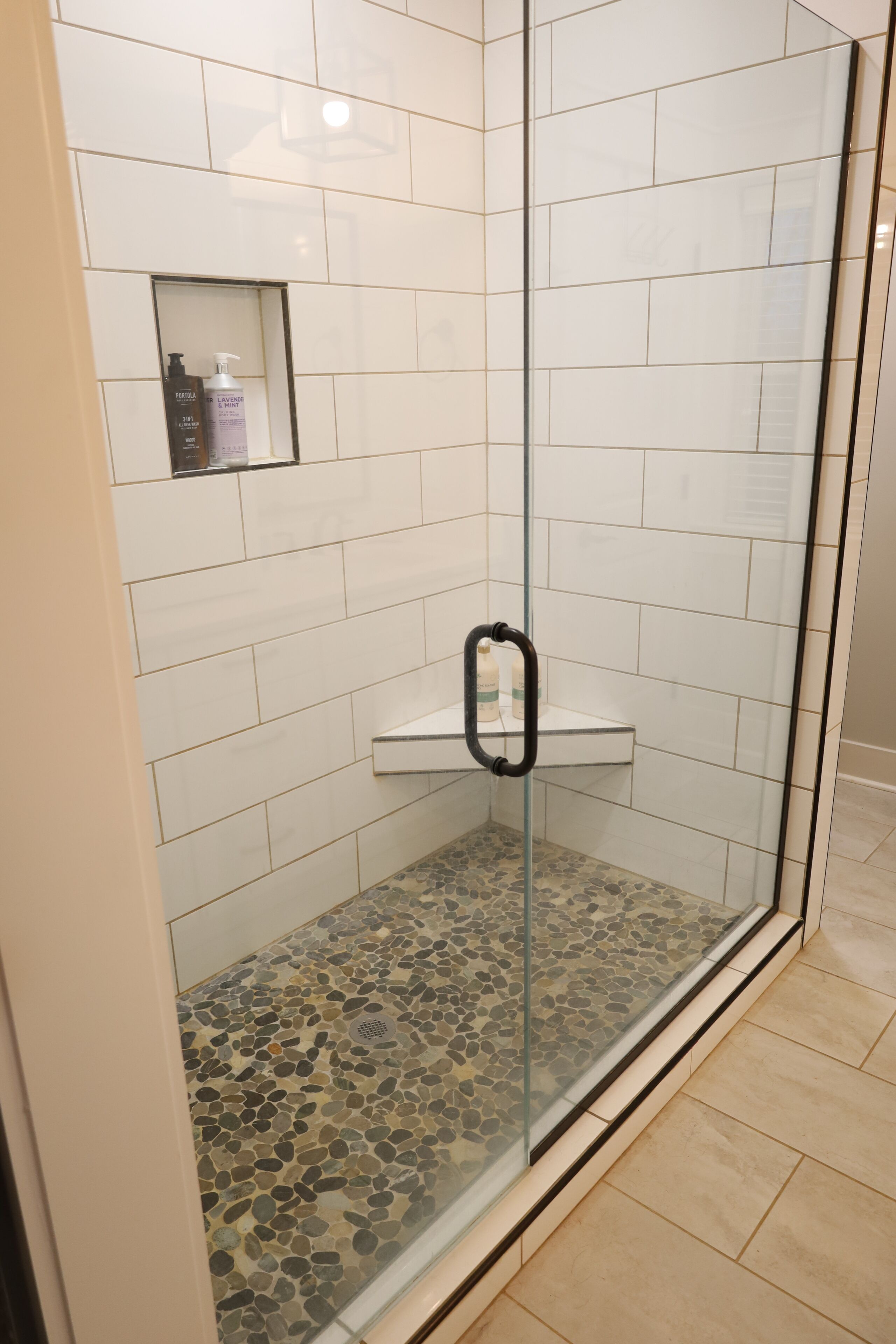 A glass-enclosed shower with a pebble-tiled floor and a shelf with toiletries.