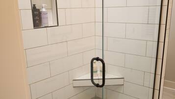 A glass-enclosed shower with a pebble-tiled floor and a shelf with toiletries.