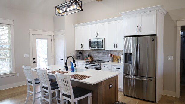 A modern kitchen with white cabinetry, stainless steel appliances, and a central island with chairs. - Modern Family-sized Country Gem near Chattanooga with relaxing balcony & deck! (Ringgold)