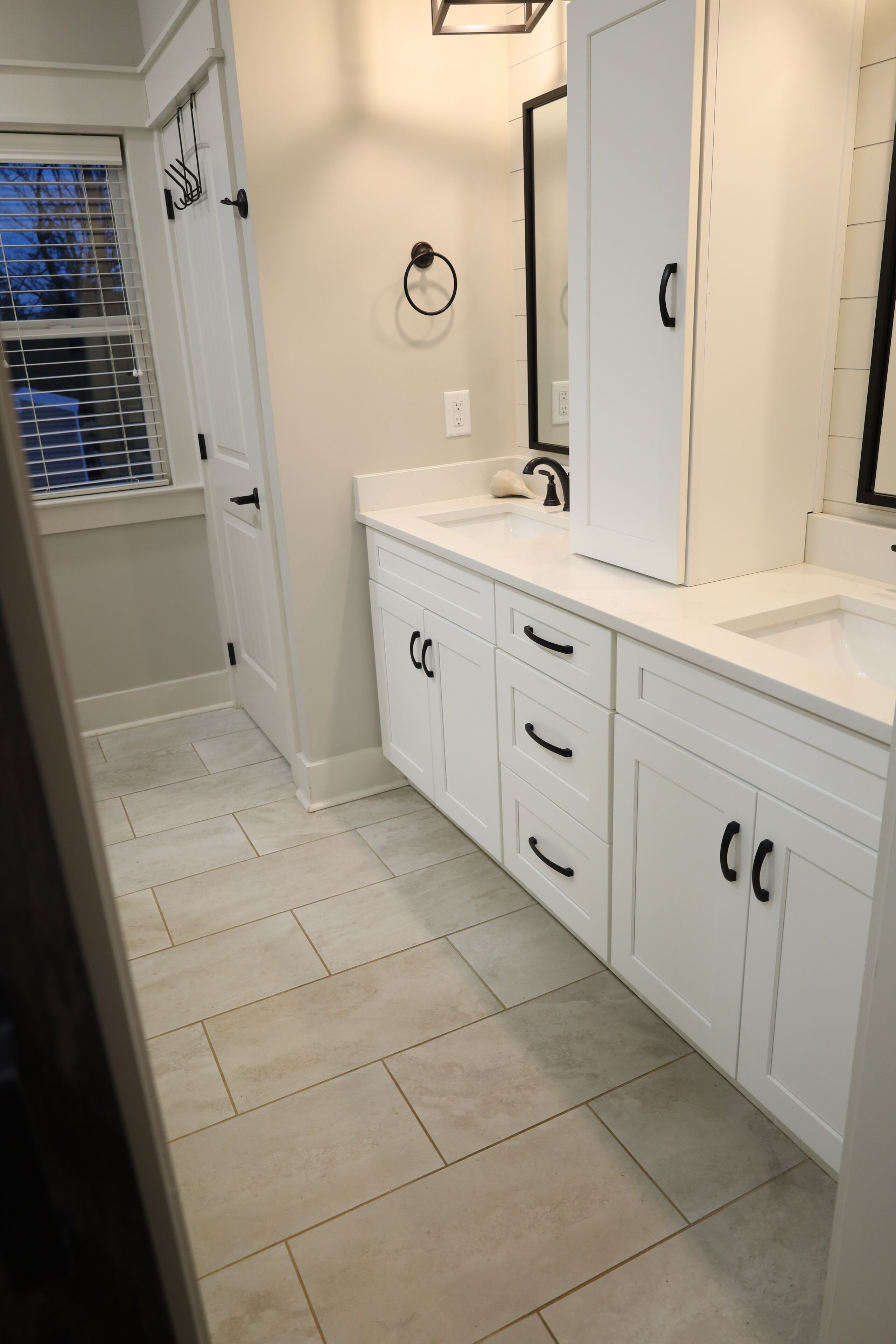 A modern bathroom with white cabinetry, a large mirror, and a window with blinds.