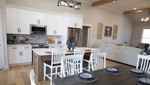 A modern kitchen with white cabinets, a stainless steel refrigerator, and a dining area with a dark wooden table and white chairs. - Modern Family-sized Country Gem near Chattanooga with relaxing balcony & deck! (Ringgold)