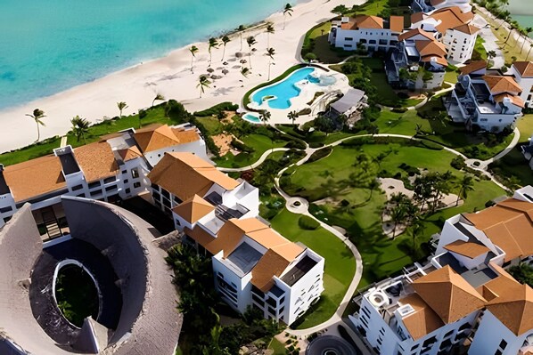 An aerial view of a resort with multiple buildings, a beach, and a swimming pool.