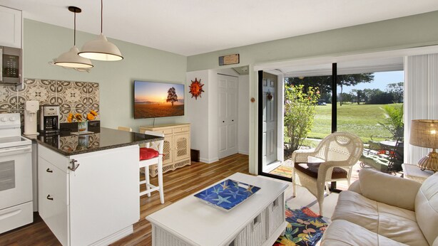 A modern kitchen with white cabinetry, a coffee machine, and a dining area with a white chair and table. - Vibrant 1bed/1bath Golf Course Front in the Meadows (Sarasota)