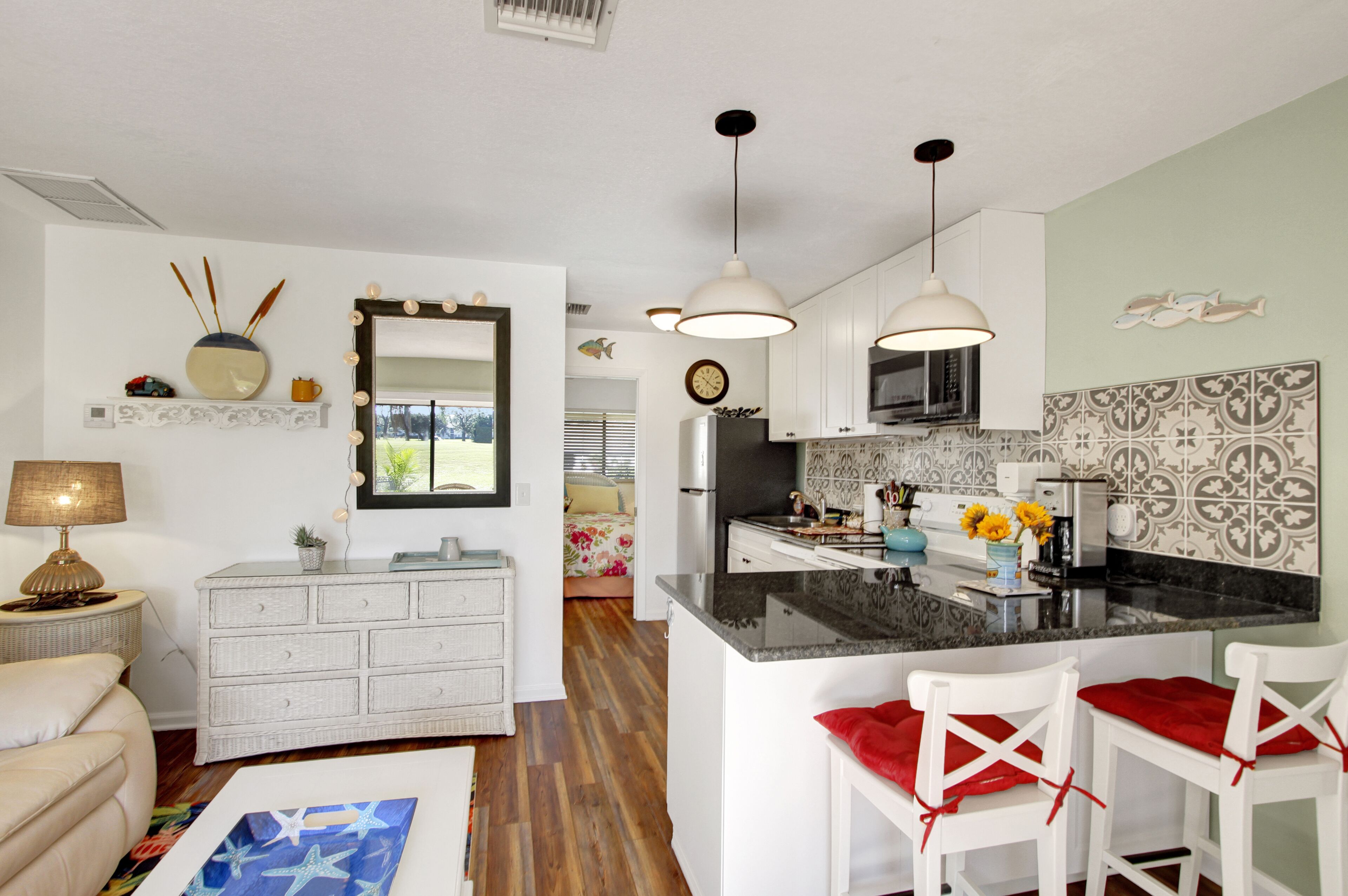 Cocina moderna con armarios blancos, una isla central con cojines rojos, iluminación colgante y un salpicadero decorativo.