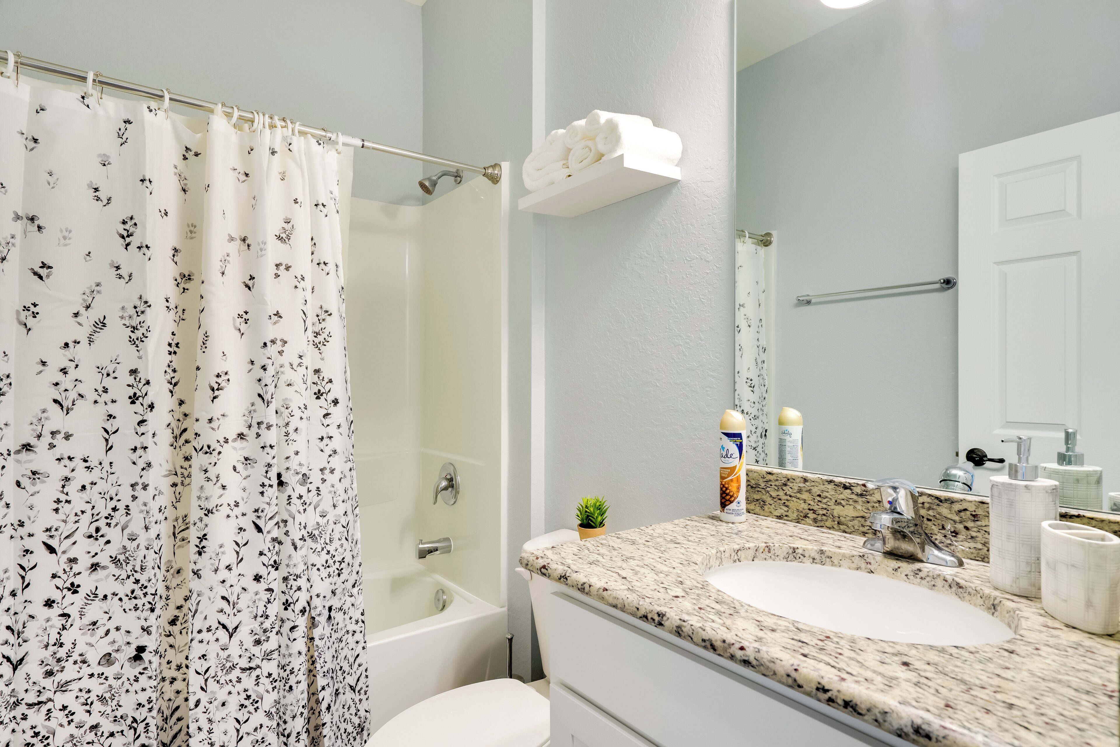 A bathroom with a shower curtain, a bathtub, a sink with a granite countertop, and a mirror.