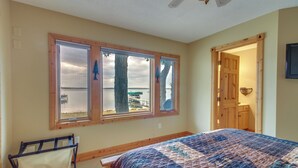 Un dormitorio con una cama grande, una ventana con vista al agua y una puerta que da a otra habitación.