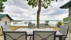 Una terraza con mesa y sillas que da a un lago, con muelles y barcos al fondo.