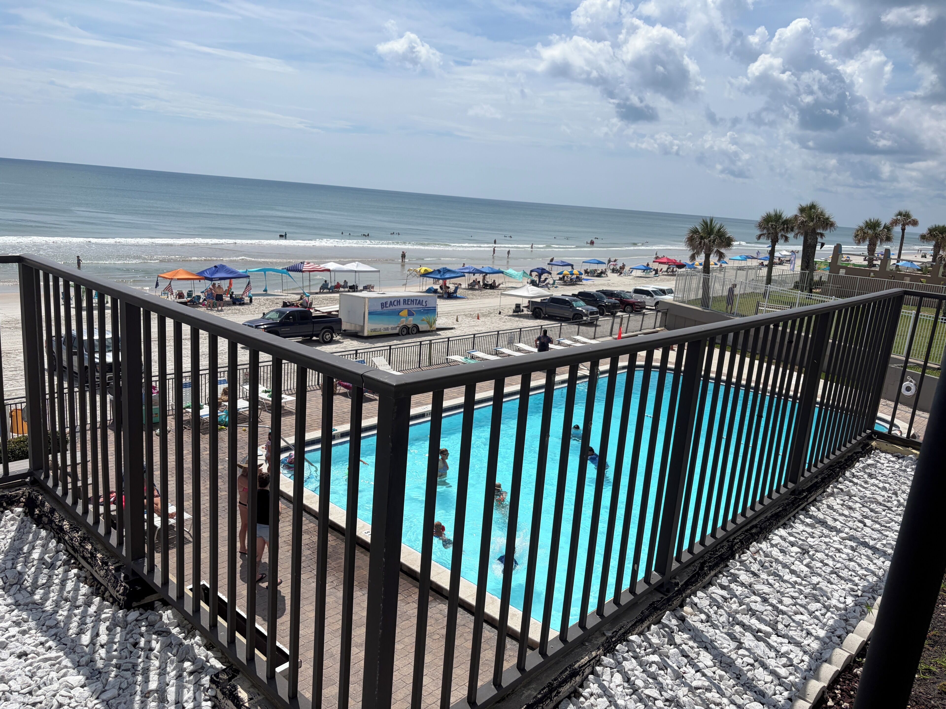 Une piscine avec vue sur la plage, un service de location de matériel de plage et une terrasse clôturée.