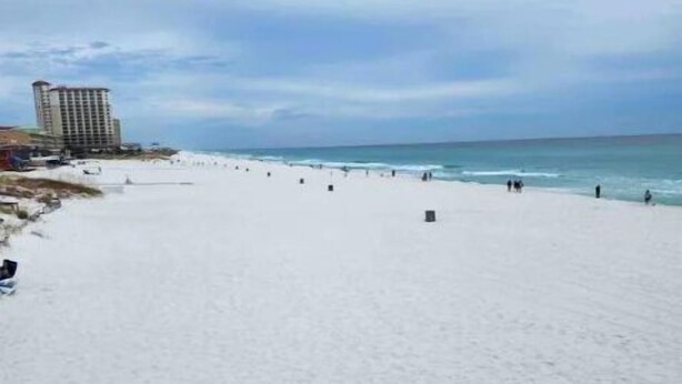 Una playa amplia y arenosa, con algunas personas y un edificio al fondo.