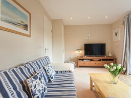 Una sala de estar con un sofá a rayas, un mueble de televisión de madera y una mesa con un jarrón de flores.