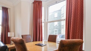 A dining area with a round wooden table, six brown upholstered chairs, and red patterned curtains.