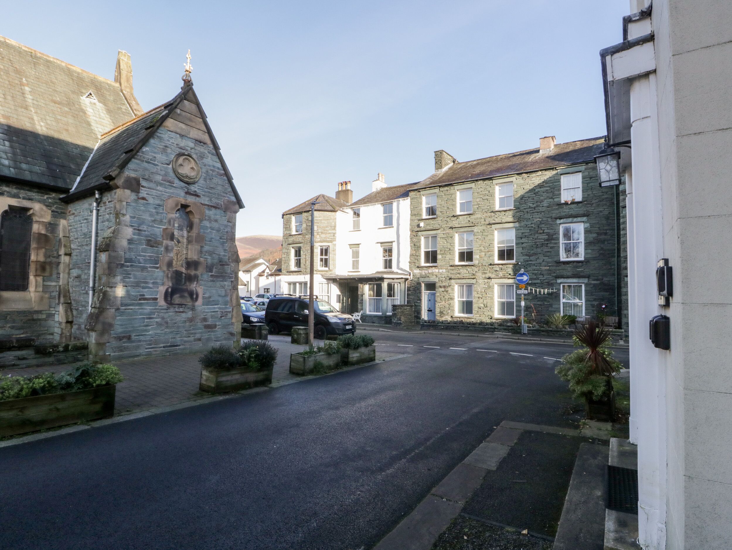 A street with stone buildings, a church, and parked cars.