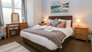 A neatly arranged bedroom with a large bed, bedside tables, a dresser, a mirror, and a painting on the wall.