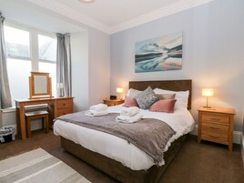 A neatly arranged bedroom with a large bed, bedside tables, a dresser, a mirror, and a painting on the wall.