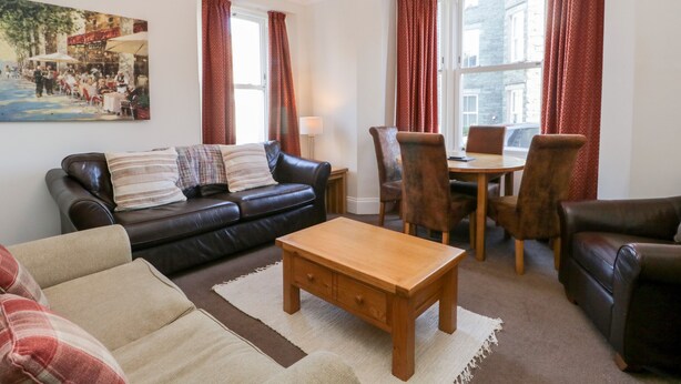 A living room with a sofa, a wooden coffee table, and a dining table with chairs.
