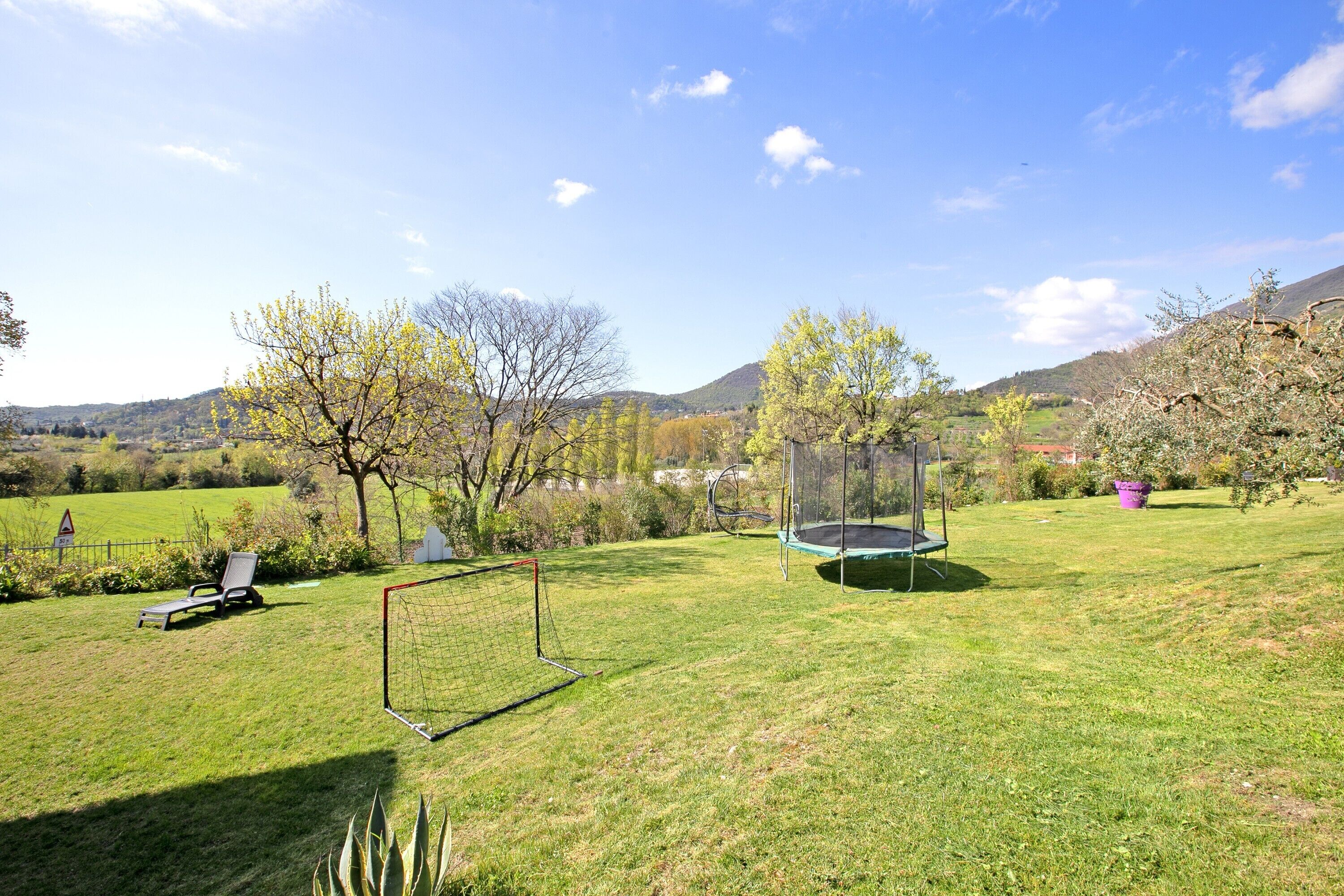 Un espacio al aire libre con césped, un trampolín, un arco de fútbol y una silla.