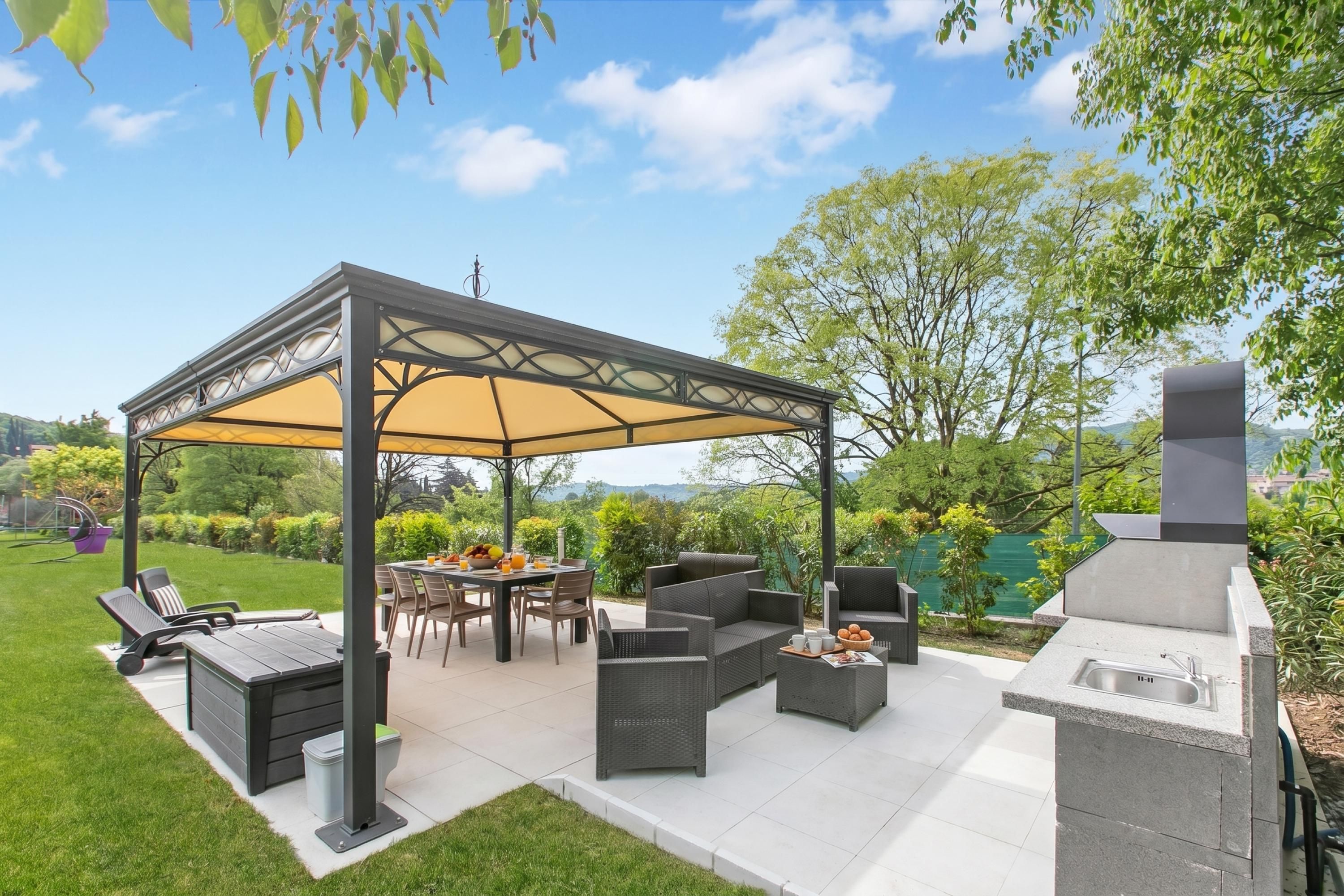 An outdoor patio with a covered seating area, a dining table, and a barbecue grill.